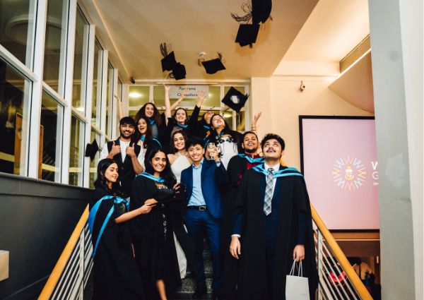 a group of graduates standing on a set of stairs, throwing their graduation caps into the air