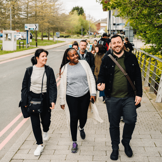 A group of students walking on Warwick main campus looking to their left talking and laughing 